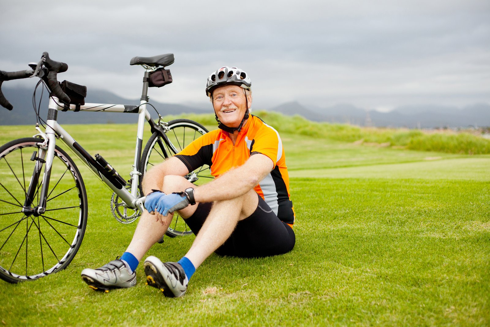 senior cyclist sitting next to bike wearing helmet